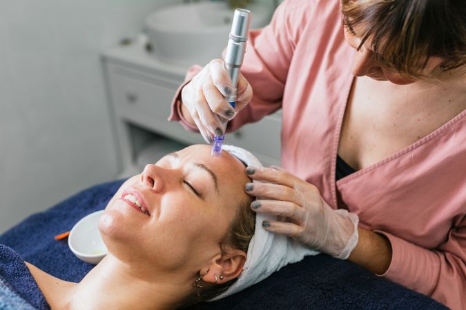 Crop cosmetologist doing microdermabrasion procedure of face of client
