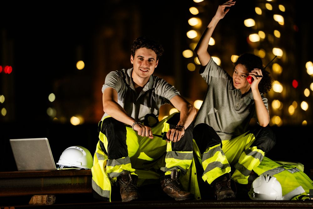 Engineer team sit for taking a break holding walkie talkie calling colleauge at night. Refinery worker at oil factory, working overtime, petroleum chemical industry