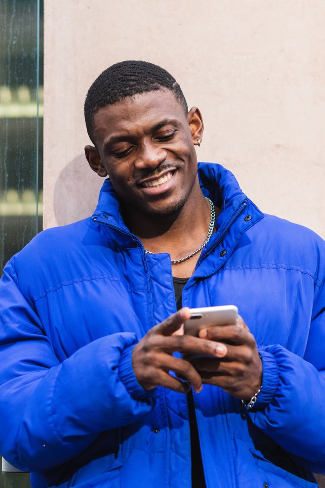 Cheerful stylish Black man chatting on social media on cellphone
