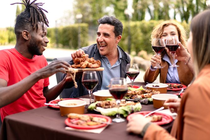 Friends share a laugh over a sumptuous outdoor meal food, toasting with glasses of red wine