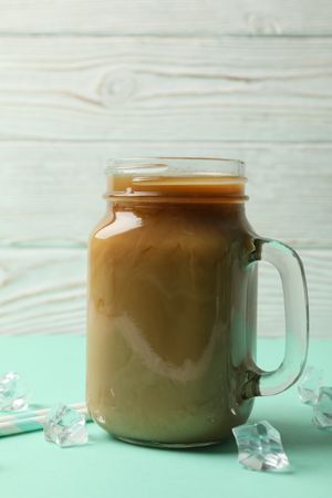 Jar of ice coffee, ice cubes and straws on mint table