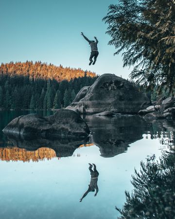 Person jumping on rock with reflection in lake water
