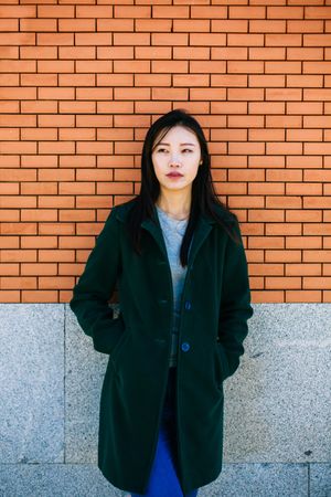 Pensive Asian woman leaning on brick wall