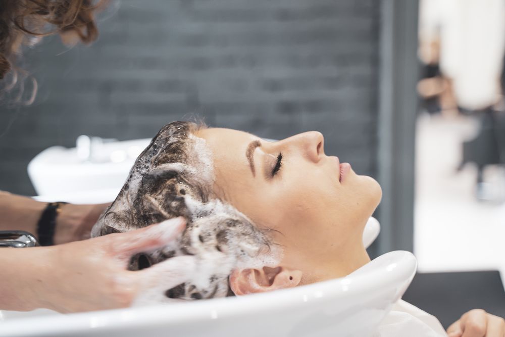 Stylist washing hairs to young woman
