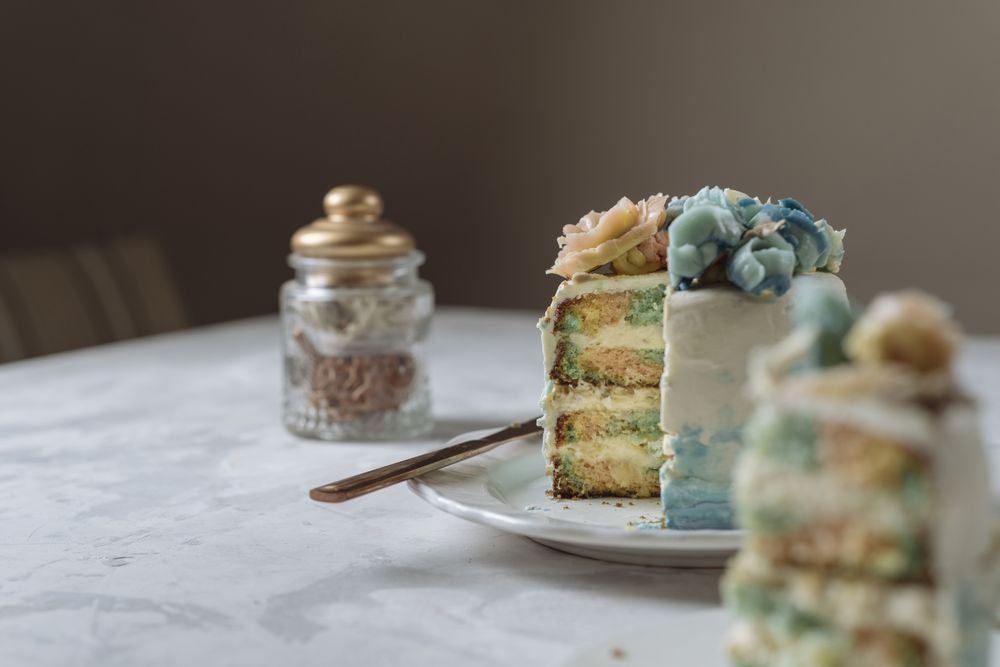 Portion of rainbow cake, filled with chantilly cream, and decorated with buttercream flowers