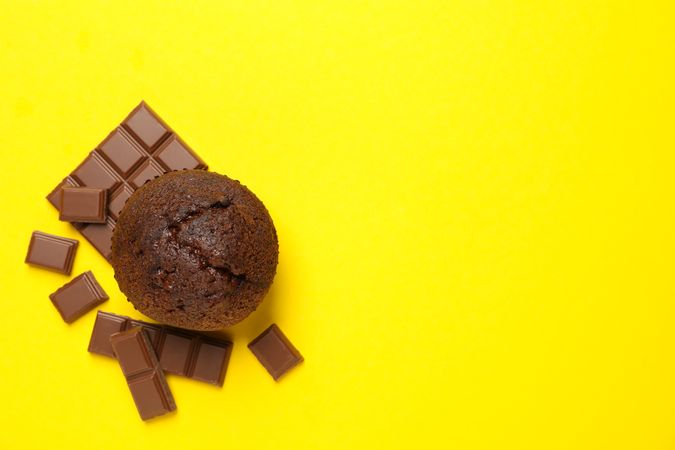 Tasty muffin and chocolate on yellow background, top view