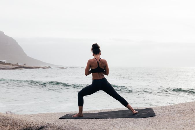 Back of female stretching while facing the ocean