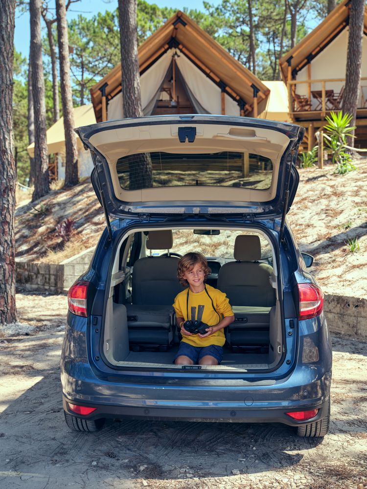 Boy sitting in car trunk and holding binoculars