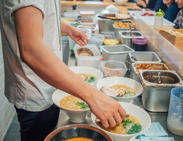 Young male cook serving bowls with ramen