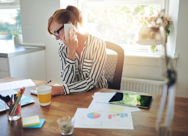 Busy woman in striped shirt taking phone call at her desk