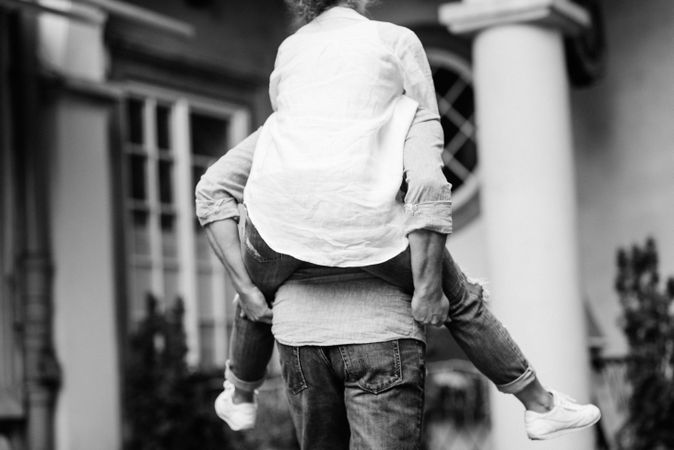 Grayscale photo of man holding woman on his back