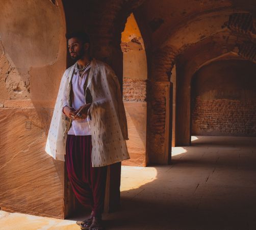 Portrait of man wearing traditional clothing standing beside pillar looking away