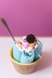 Close up of a blue rolled ice cream decorated with chocolates, cream and a cookie