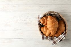 Top view of wicker basket with croissants on wooden table, copy space