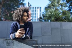 Black man in cardigan leaning forward outdoors on sunny day holding smartphone 5aX3Y8