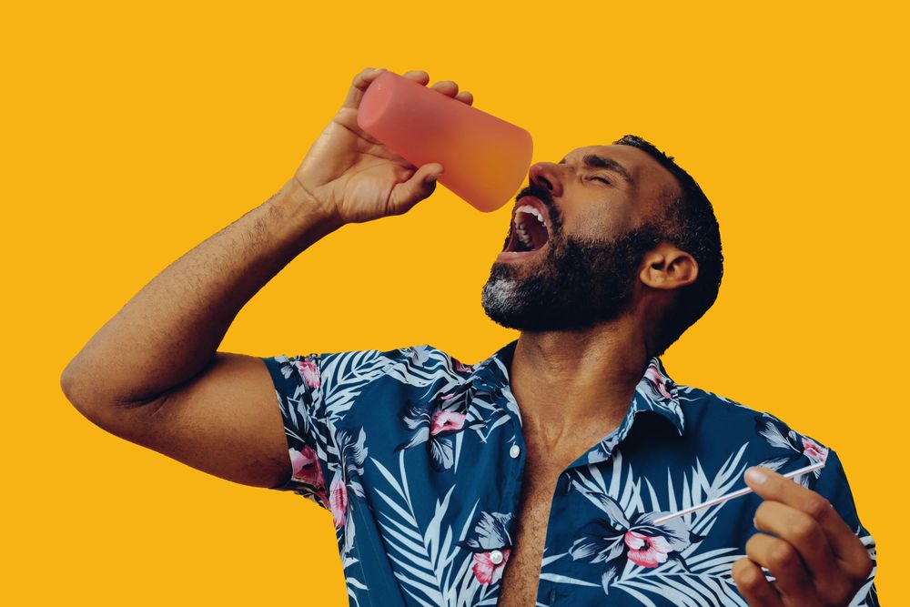 Male emptying a drink from orange cup into his mouth in yellow studio