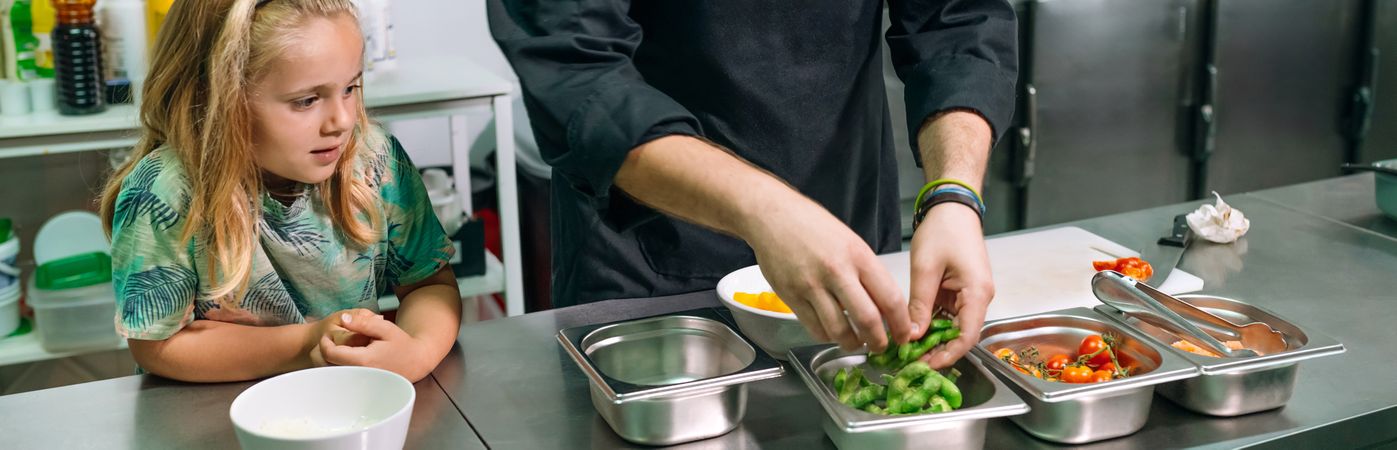 Banner of chef preparing food with a happy young girl watching him in a professional kitchen