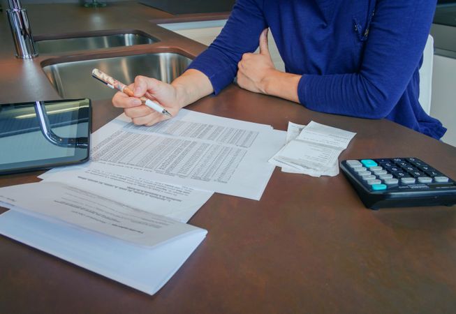Woman reviewing her monthly bills scattered on kitchen counter