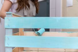 Woman paining wooden box in blue color with roller