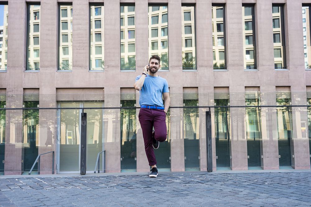 Bearded man leaning on glass railing outside talking on mobile phone