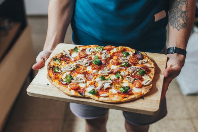 Tattooed man holding wooden board with pizza