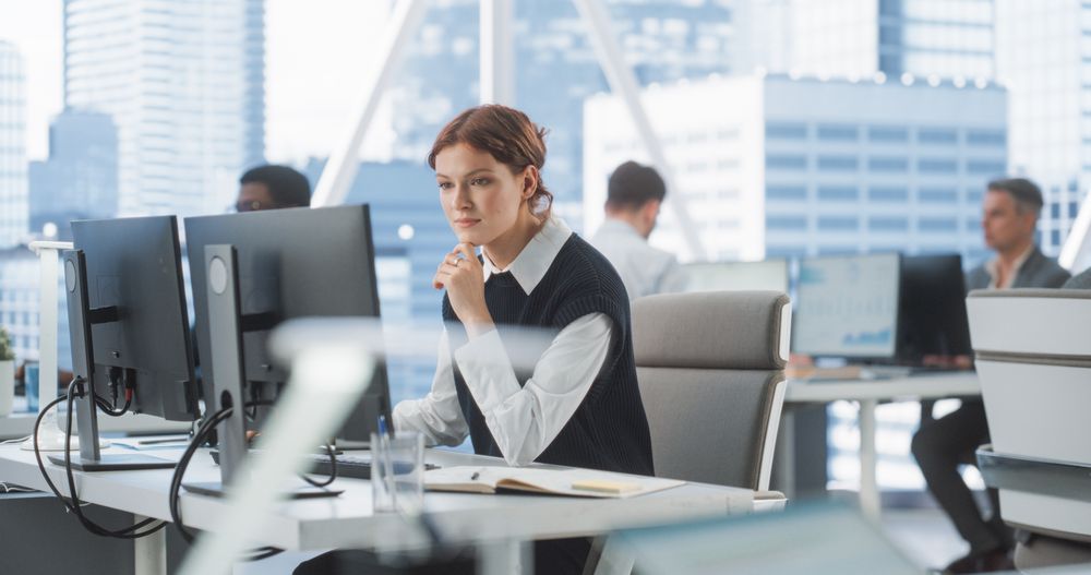 Happy Female Account Manager Typing On Desktop Computer In Diverse Corporate Office With Megapolis Window View.