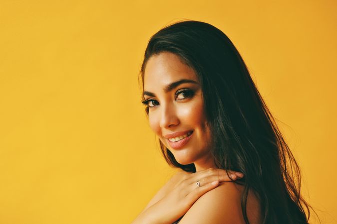Happy Hispanic woman looking around at camera in yellow room with her hand on her shoulder