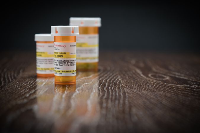 Variety of Non-Proprietary Prescription Medicine Bottles on Reflective Wooden Surface.