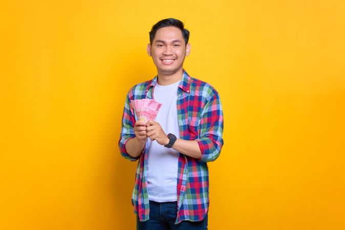 Asian man holding cash with both hands in studio shoot