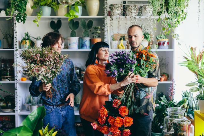Woman and two men holding bouquets in the flower shop.