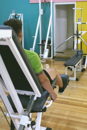 Rear view of fit male in green t-shirt working out using leg extension machine
