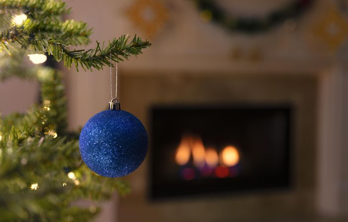 Blue Christmas ornament with glowing fireplace in background