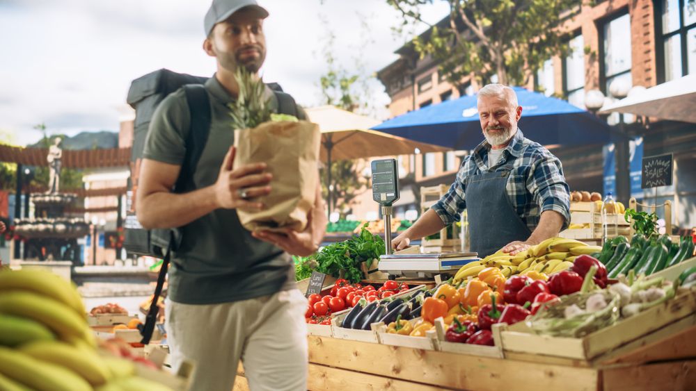 Cheerful Street Vendor Handing Over a Recycled Paper Bag with Fresh Produce