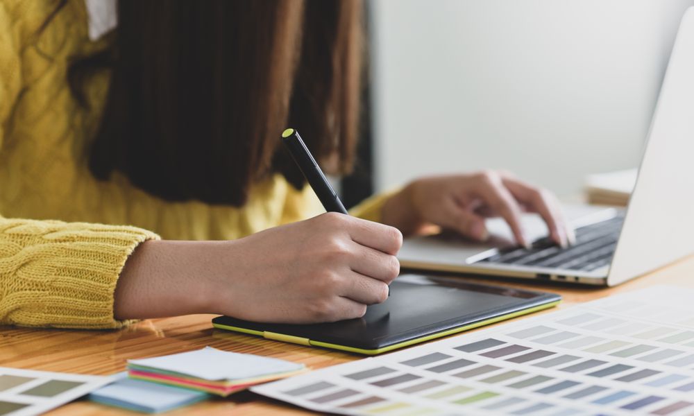 A woman writing on digital board with pen and working on laptop