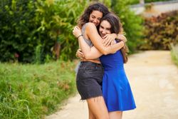 Two smiling friends embrace after meeting in the park