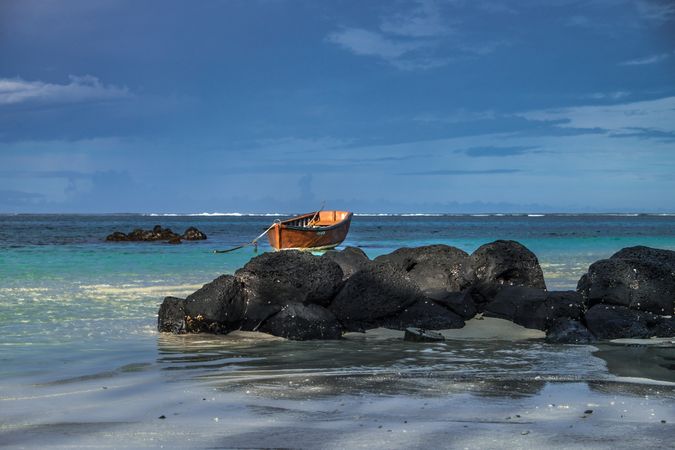 Red boat anchored in shallow lagoon in Mauritius near volcanic rock