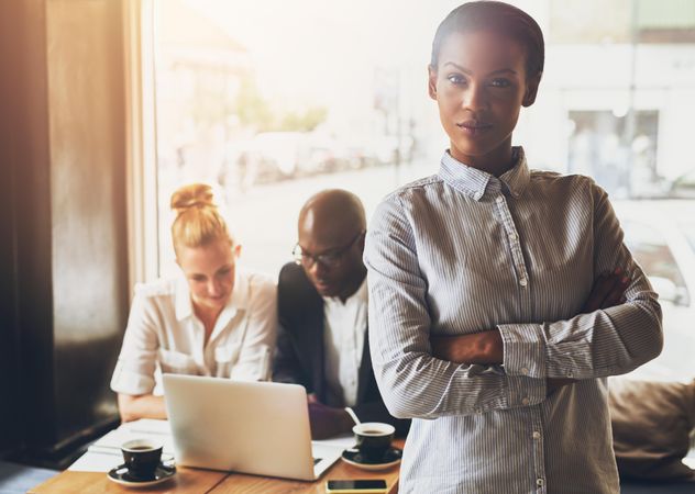 Portrait of Black businesswoman pictured with her arms crossed in front of her colleagues