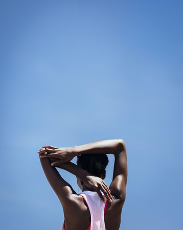 Rear view of a woman stretching arm muscles against blue sky outdoors
