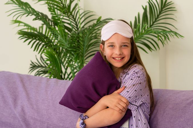 Happy girl hugging pillow, seated on purple couch