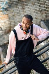 Happy male in overalls and pink hoodie leaning on railing of stairs outside