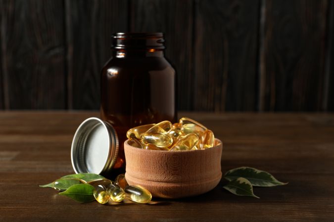 Wooden bowl with omega pills on dark background