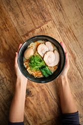 Crop person serving plate with ramen