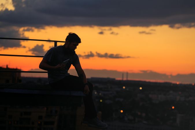 Out line of male sitting on roof against a colorful dusk side