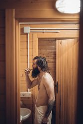Bearded man brushing teeth in wooden house