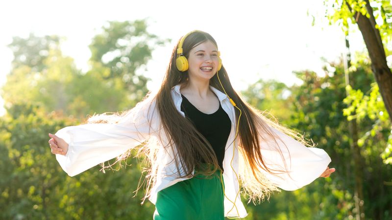 Teenage girl listening to music and dancing with headphones outdoors