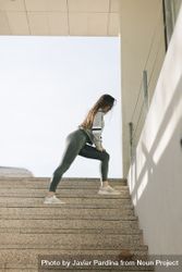 Full length side view shot of woman in grey workout pants stretching on stairs outside 0KMWZ4
