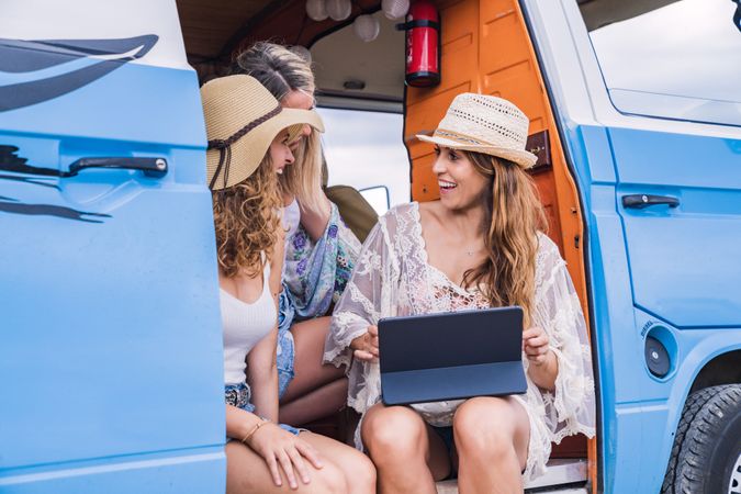 Lively women in hat speaking with tablet on knees sitting in open car