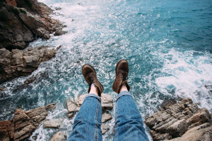 Hiker sitting on rocks overlooking ocean in leather boots, landscape
