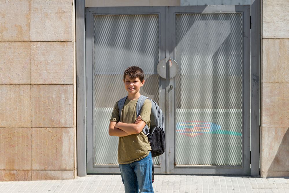 Smiling child carrying his backpack standing in front of the school