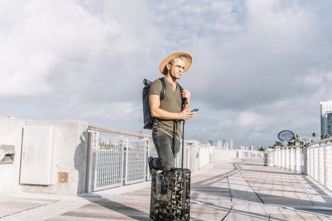 man using cell telephone, with a knee on his carrying luggage